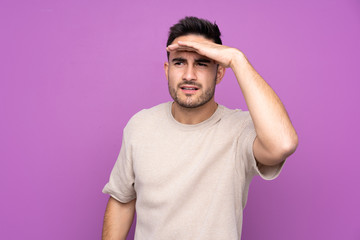 Fototapeta premium Young handsome man over isolated purple background looking far away with hand to look something