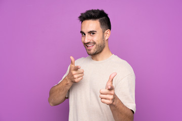 Young handsome man over isolated purple background pointing to the front and smiling