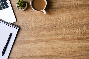 desk office with laptop, blank notepad, coffee cup and pen on wood table. Flat lay top view copy spce.