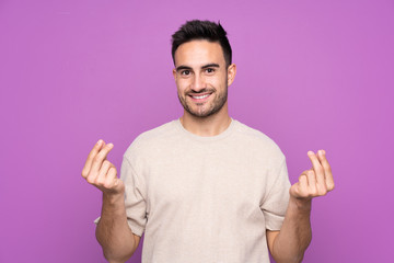 Young handsome man over isolated purple background making money gesture