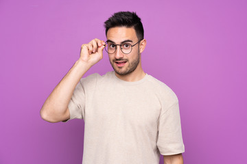 Young handsome man over isolated purple background with glasses and surprised