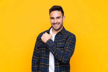 Young handsome man over isolated yellow background celebrating a victory