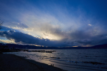 Obraz premium Lake in a windy day, landscape where sunlight can be seen through a gap in a cloudy sky.
