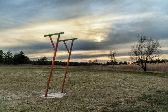 Metal parallel bars in the middle of the field. The only gym available during the quarantine due to corona virus. No people around. Equipment is next to the forest. Sunset view. Village sport.