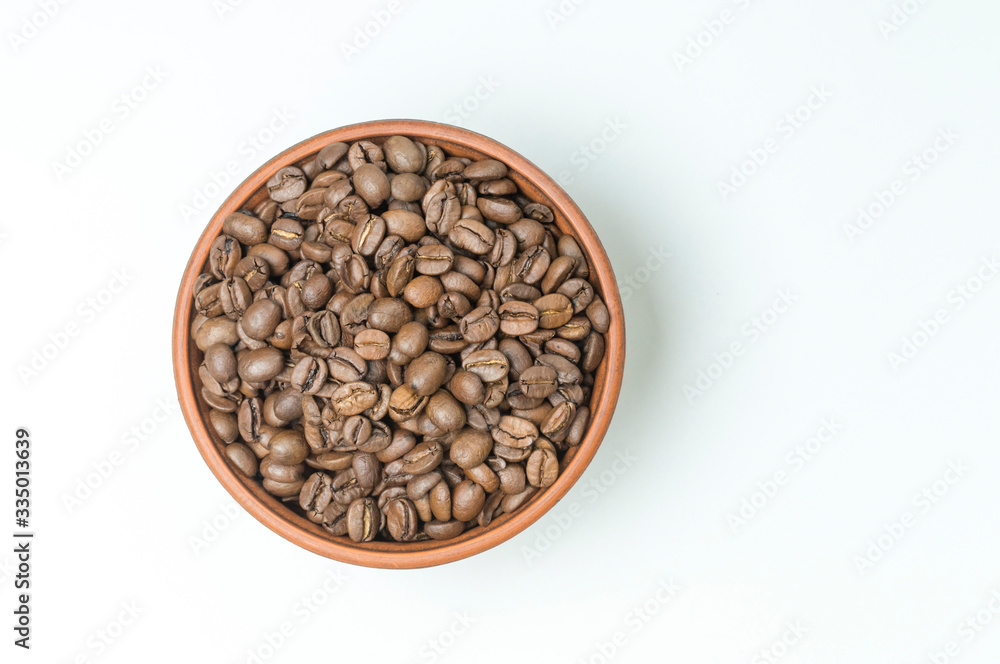 Wall mural roasted coffee beans in a clay cup on a white background top view