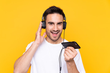 Young man over yellow background listening music with a mobile and singing