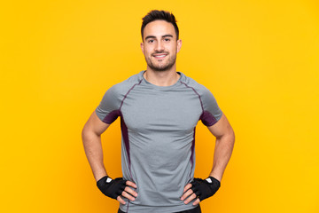 Sport man over isolated yellow wall posing with arms at hip and smiling
