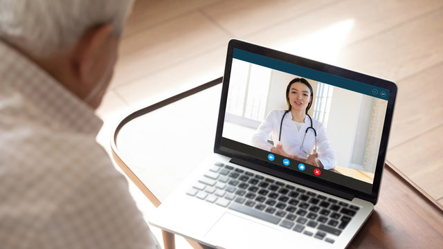 Close up of mature man have video call consult with female nurse using laptop webcam, elderly male patient sit at home talk speak with doctor or physician, discuss symptoms with gp on computer online
