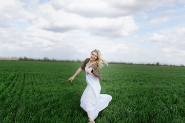 Fototapeta na wymiar blonde girl in a white dress sits on the green fresh spring grass, blue sky