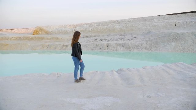 Pretty brunette girl in a black jacket walking on the kaolin quarry. Side view. Slow motion.