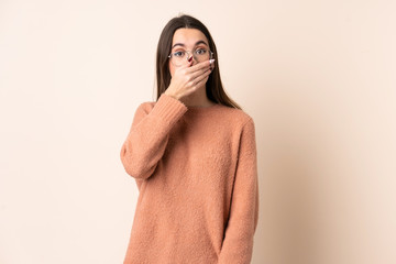 Young woman over isolated beige background covering mouth with hand