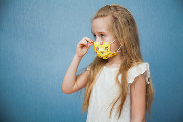 Little girl putting on protective medical mask on blue background.