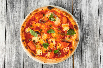 Pizza with tomatoes, cheese and basil on wooden background. Closeup, top view