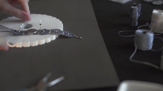 Lifestyle concept, reinvent your life and your job: close-up detail in low angle view of woman hands making macrame knotted bracelet with the fingers knotting the nylon thread on the kumihimo