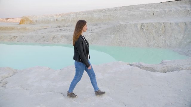Pretty brunette girl in a black jacket walking on the kaolin quarry. Slow motion.