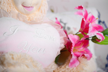 Big soft plush happy toy bear with a heart in his hands and flowers sits as a gift on a soft sofa and declares his love