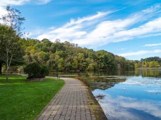 Walking trail through Twin Lakes in the Laurel Highlands of Pennsylvania with green trees, grass and bright blue skies with clouds reflecting in the water.  Beautiful nature landscape.
