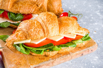 Homemade croissant sandwiches with ham, cheese, fresh vegetables and herbs,