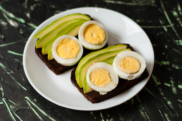 Sandwiches with avocado and egg on a dark background, top view