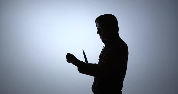 Silhouette of a criminal wipes a knife with his clothes