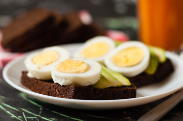 Black whole grain bread, sandwiches with eggs and avocados, multifruit juice in a tall glass. Concept proper nutrition