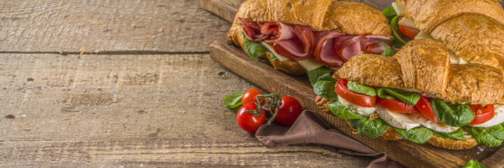 Homemade croissant sandwiches with ham, cheese, fresh vegetables and herbs,