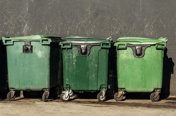 Green garbage containers stand in the city against a concrete wall. Disposal during a pandemic