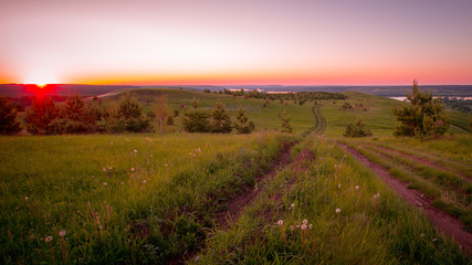 Fototapeta na wymiar country road on green hills in the rays of the setting sun