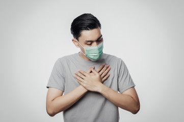 Young Asian Man in hygienic mask suffering sore throat, 2019-nCoV or coronavirus. Airborne respiratory illness such as pm 2.5 fighting and flu. Studio shot isolated on white background.