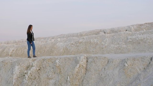 Young long haired pretty thing girl in a black jacket walking on the kaolin quarry. Side view. Slow motion.