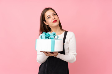 Fototapeta premium Girl holding a big cake isolated on pink background looking up while smiling