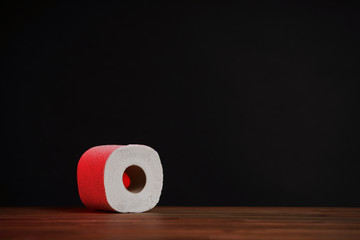 Toilet paper roll illuminated with red light. Soft hygienic paper. Wooden table on black background.