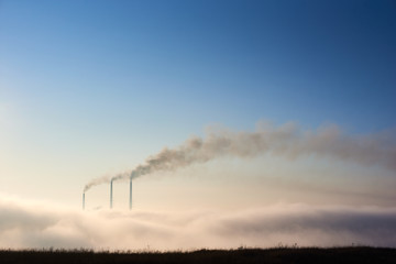Tops of three smoking stacks of thermal power station on horizon taken from the hill, pipes in...