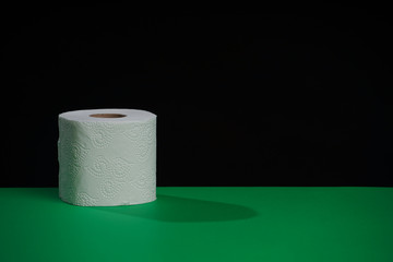 The toilet paper roll is green on a black background. Cheap toilet wipes for hygiene purposes. Soft hygienic paper.