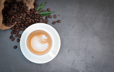 Top view coffee cup with roasted coffee beans and leaves on vintage cement table background, flat lay with copy space