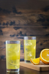 Two orange juice glass with ice cubes on wooden background