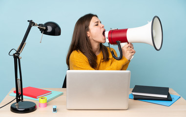 Student girl studying in her house isolated on blue background shouting through a megaphone