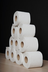 Many toilet paper rolls stacked in pyramid shape. Soft hygienic paper. Wooden table on black background