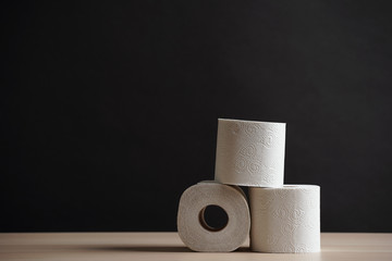Many toilet paper rolls stacked in pyramid shape. Soft hygienic paper. Wooden table on black background