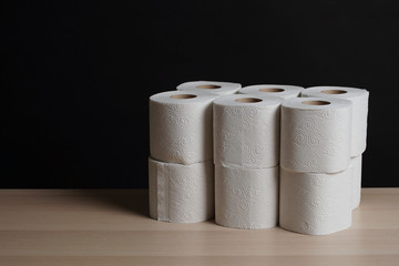 Many toilet paper rolls in a pile. Soft hygienic paper. Wooden table on black background.