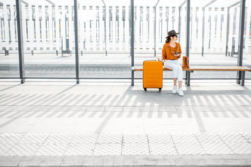 Young female traveler sitting with a suitcase at the transport stop, waiting for the tram or bus....