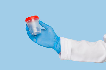 Hands of a doctor in sterile gloves hold a jar for analysis of urine or feces on a blue background. Disease prevention concept