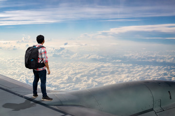 Man traveler standing on wing of airplane and looking view clouds scape 0n blue sky.