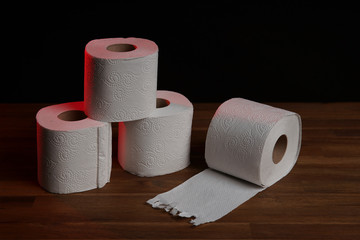 Many toilet paper rolls piled in a heap. Soft hygienic paper. Wooden table on black background.