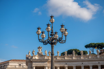 latarnia na plecyu Świętego Pitra w Watykanie. jedna z kilku ozdobnych, zabytkowych latarni . W tle piękne rzeźby otaczające cały plac - obrazy, fototapety, plakaty