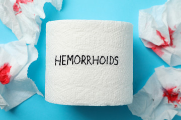 Toilet paper with Hemorrhoids and paper with blood on blue background, close up