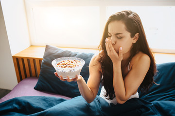 Obraz na płótnie Canvas Young beautiful woman in morning bed at home. Female person feel sick after eating breakfast cereal with milk. Feel vomiting. Disgust.