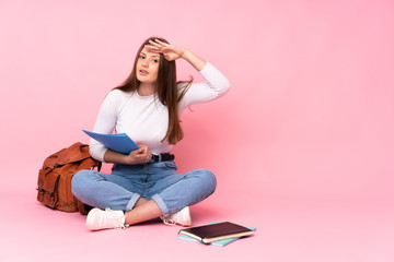 Teenager caucasian student girl sitting on the floor isolated on pink background looking far away with hand to look something