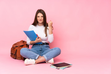 Teenager caucasian student girl sitting on the floor isolated on pink background with angry gesture