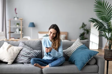 Fotobehang Online chat. Smiling woman talking on smartphone with friends while sitting on sofa at home. © BestForYou